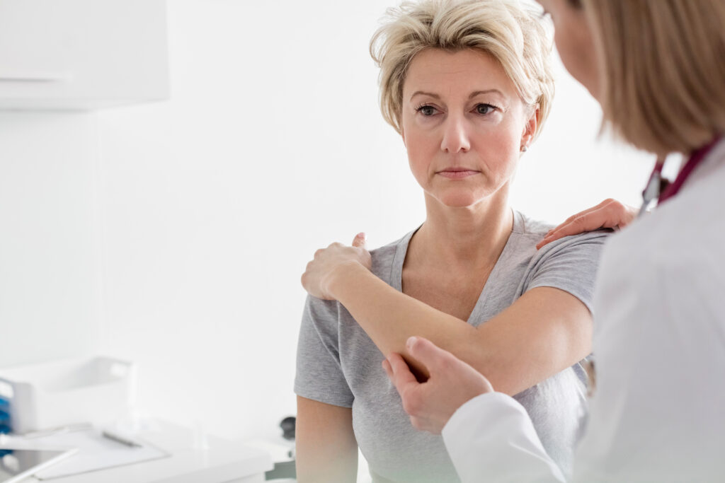 Doctor assisting mature patient in stretching her arm at hospital