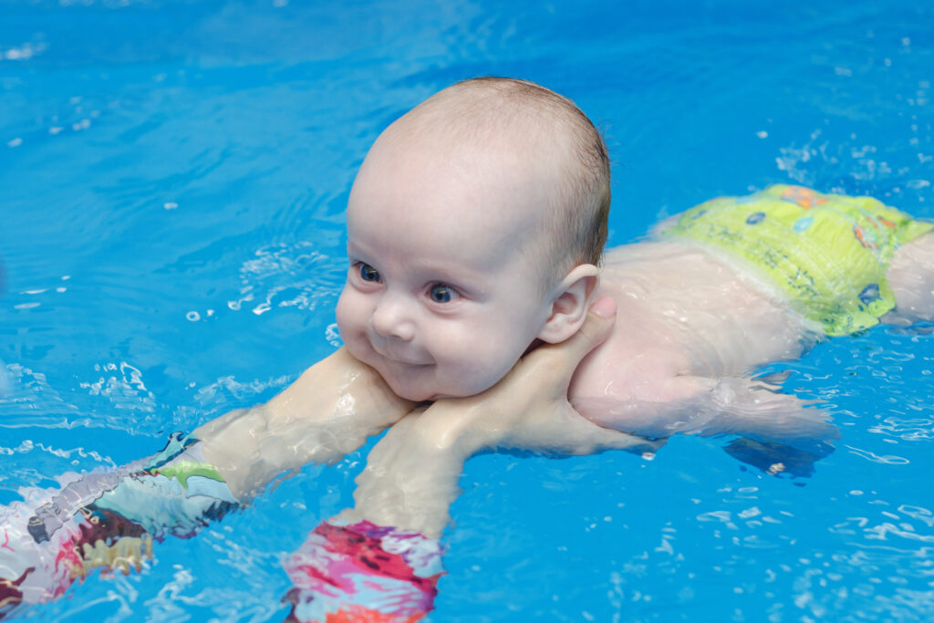 baby infant learns to swim in the pool, instructor's hands support